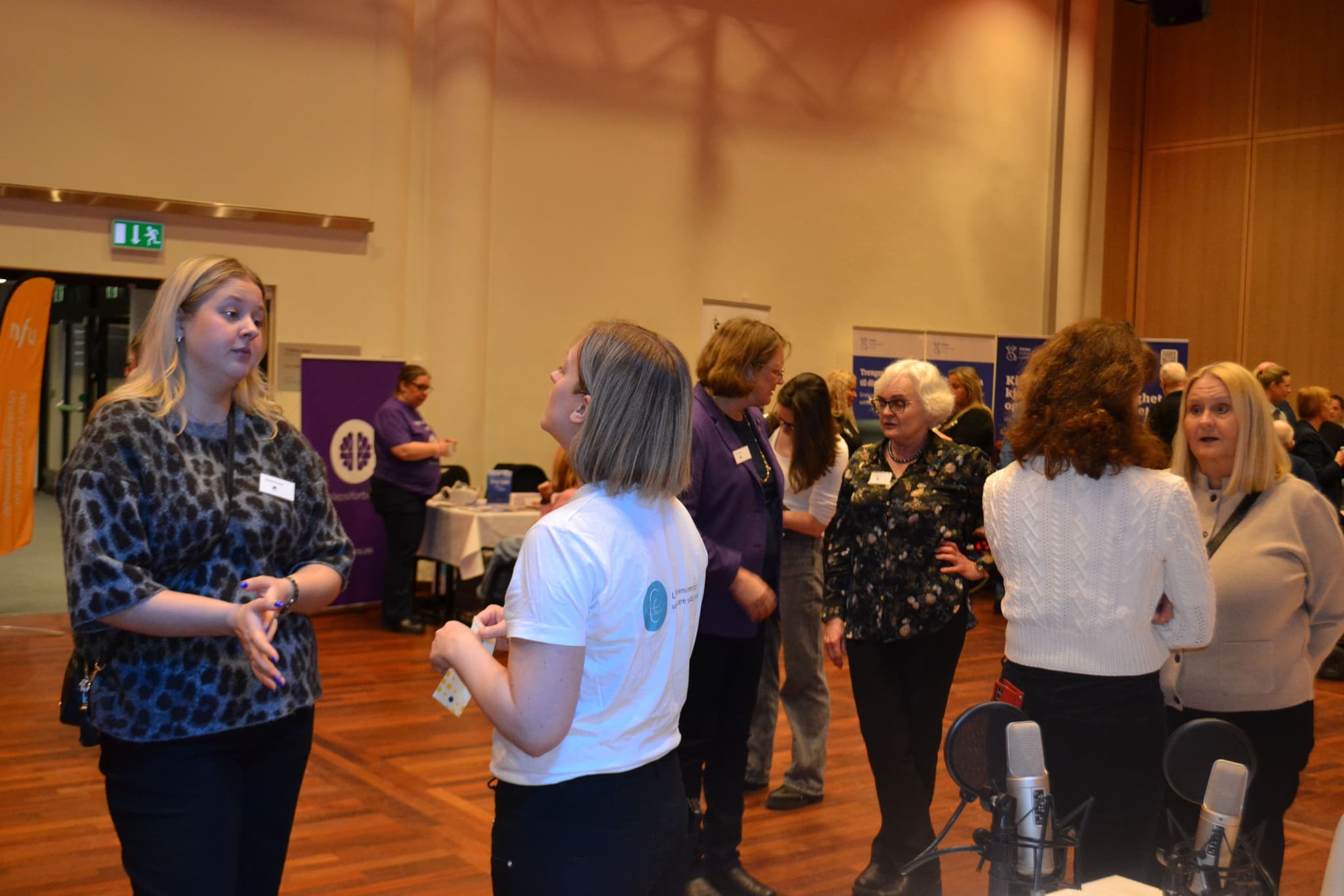 Mange personer står å snakker sammen inne i en sal.