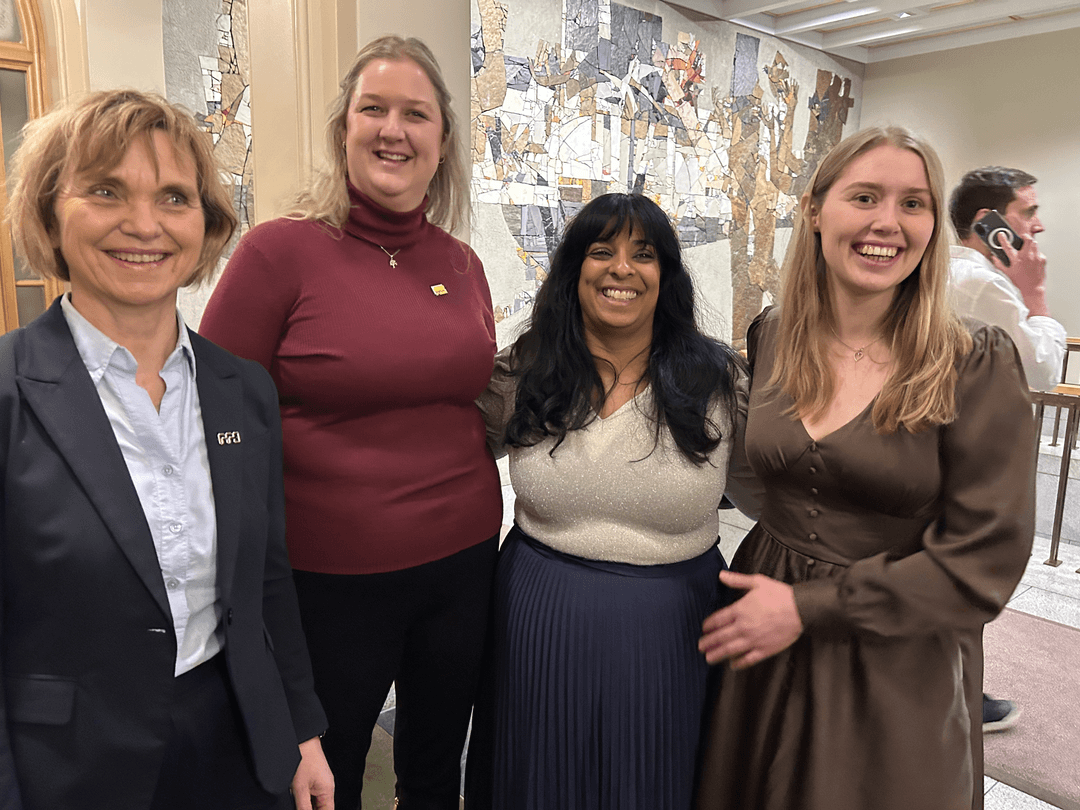 Flere personer står sammen inne i regjeringsbygget. De er dress- og kjolekledde. Alle smiler stort mot kamera.