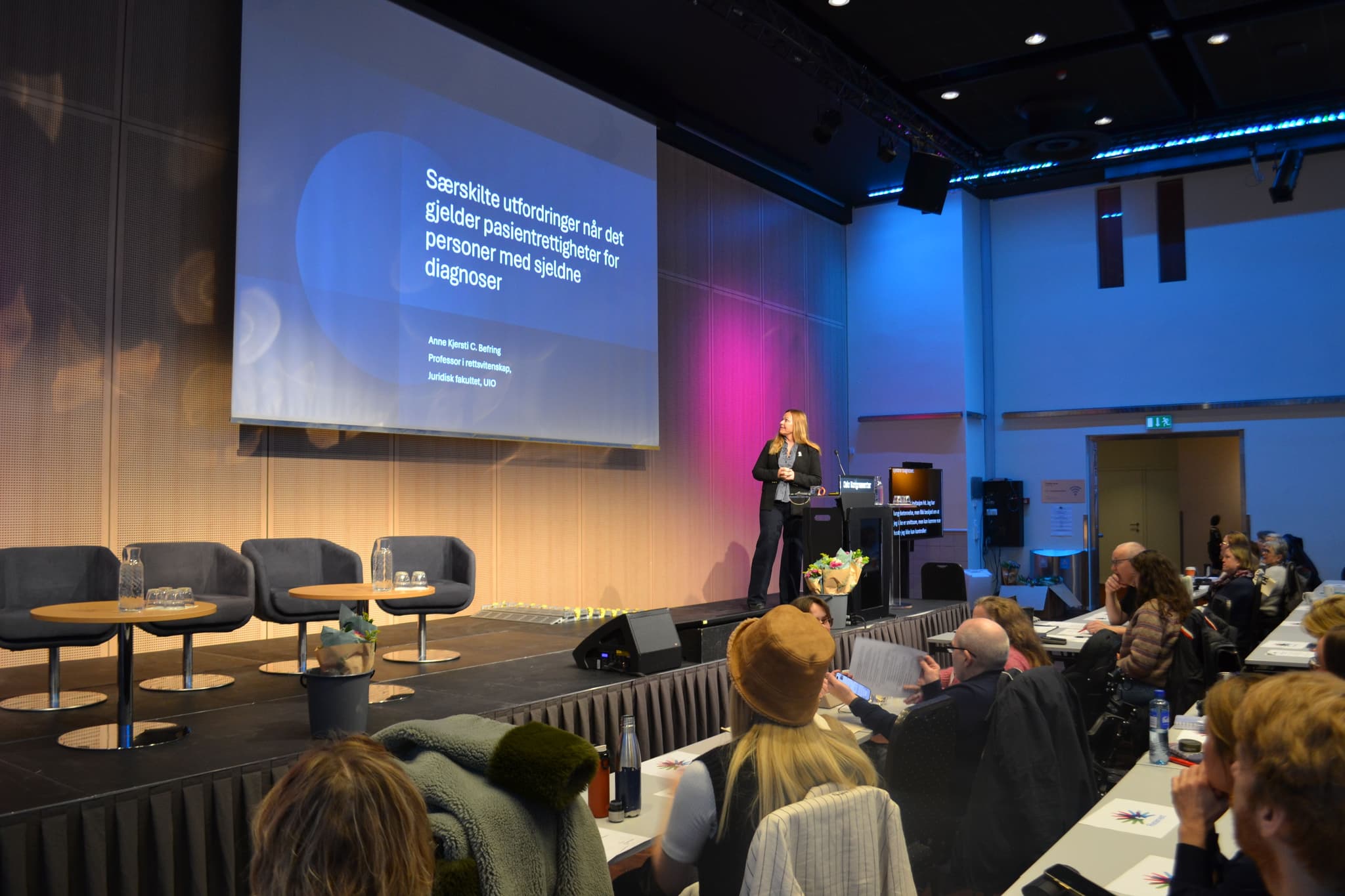 En person står på en scene foran en fullsatt sal.